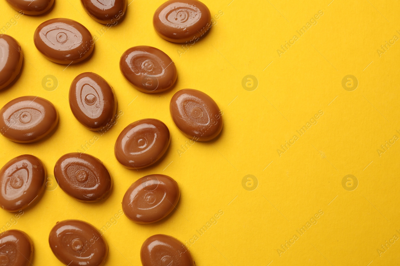 Many tasty caramel candies on yellow background, flat lay. Space for text Photo of Many tasty caramel candies on yellow background, flat lay. Space for text