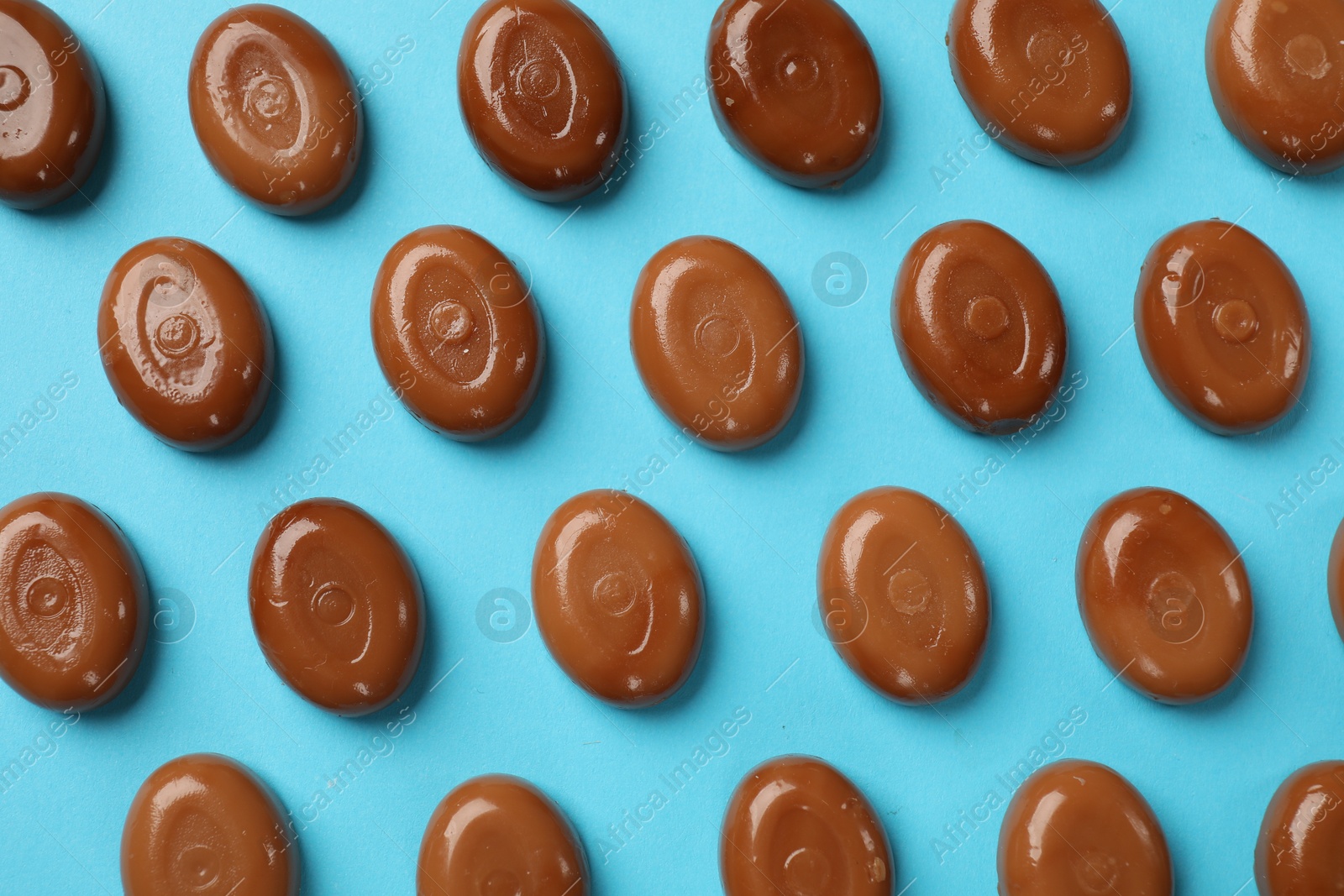 Many tasty caramel candies on light blue background, flat lay Photo of Many tasty caramel candies on light blue background, flat lay