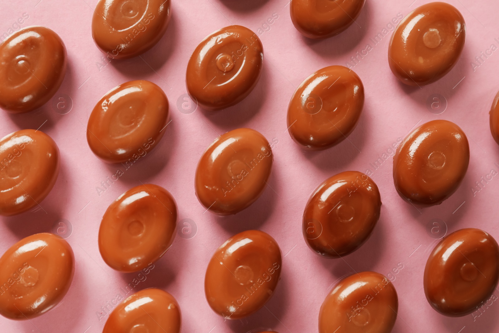 Many tasty caramel candies on light pink background, flat lay Photo of Many tasty caramel candies on light pink background, flat lay