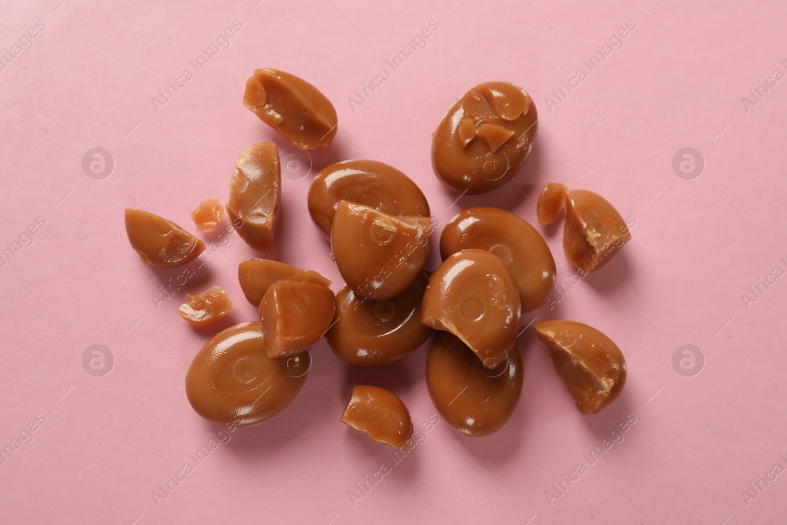 Many tasty caramel candies on light pink background, flat lay Photo of Many tasty caramel candies on light pink background, flat lay
