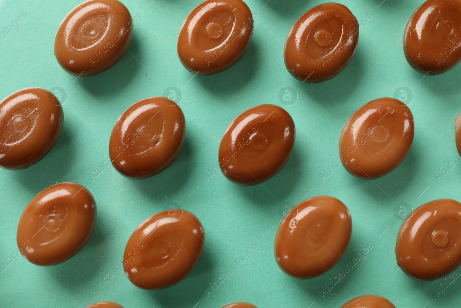 Many tasty caramel candies on turquoise background, flat lay Photo of Many tasty caramel candies on turquoise background, flat lay