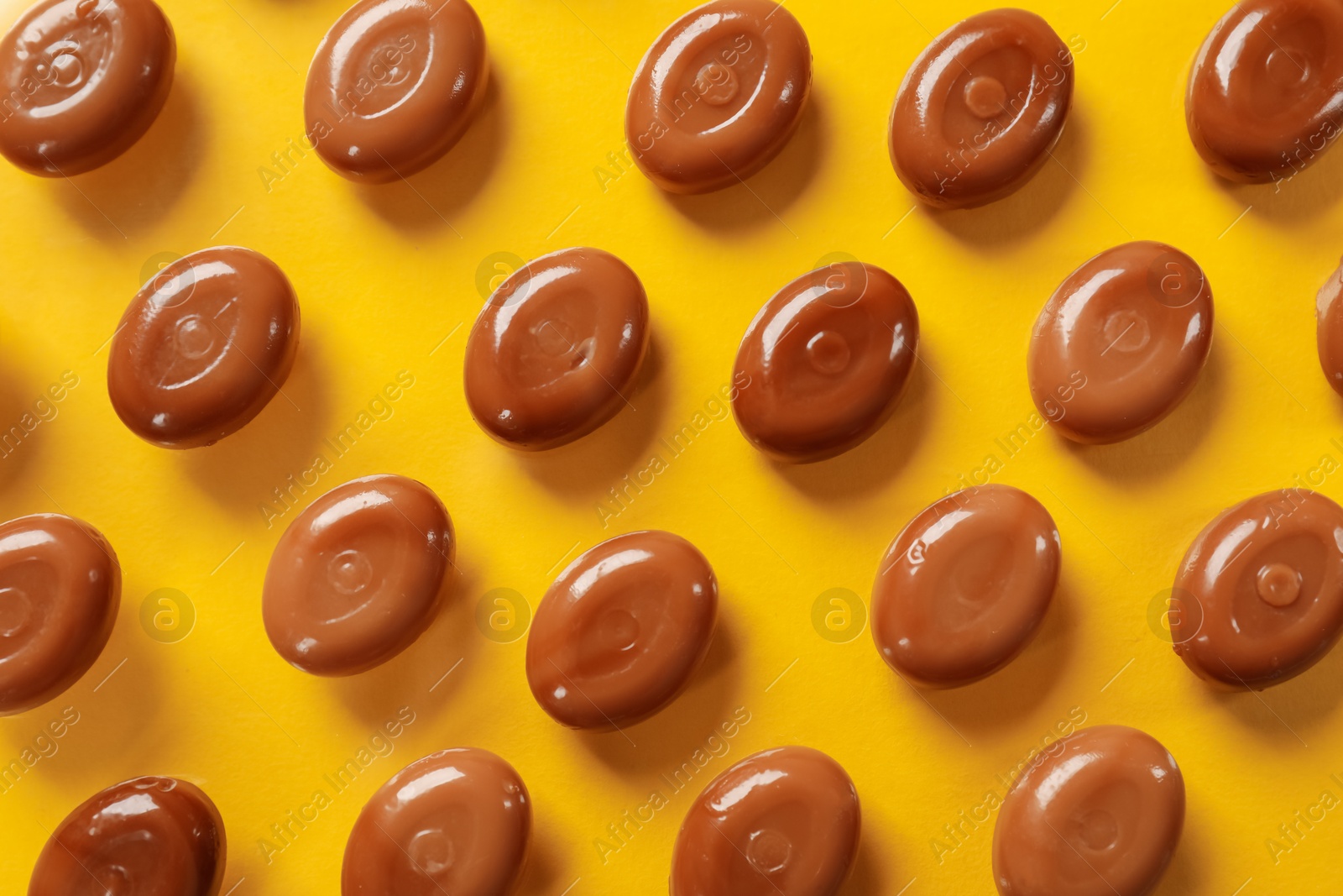 Many tasty caramel candies on yellow background, flat lay Photo of Many tasty caramel candies on yellow background, flat lay