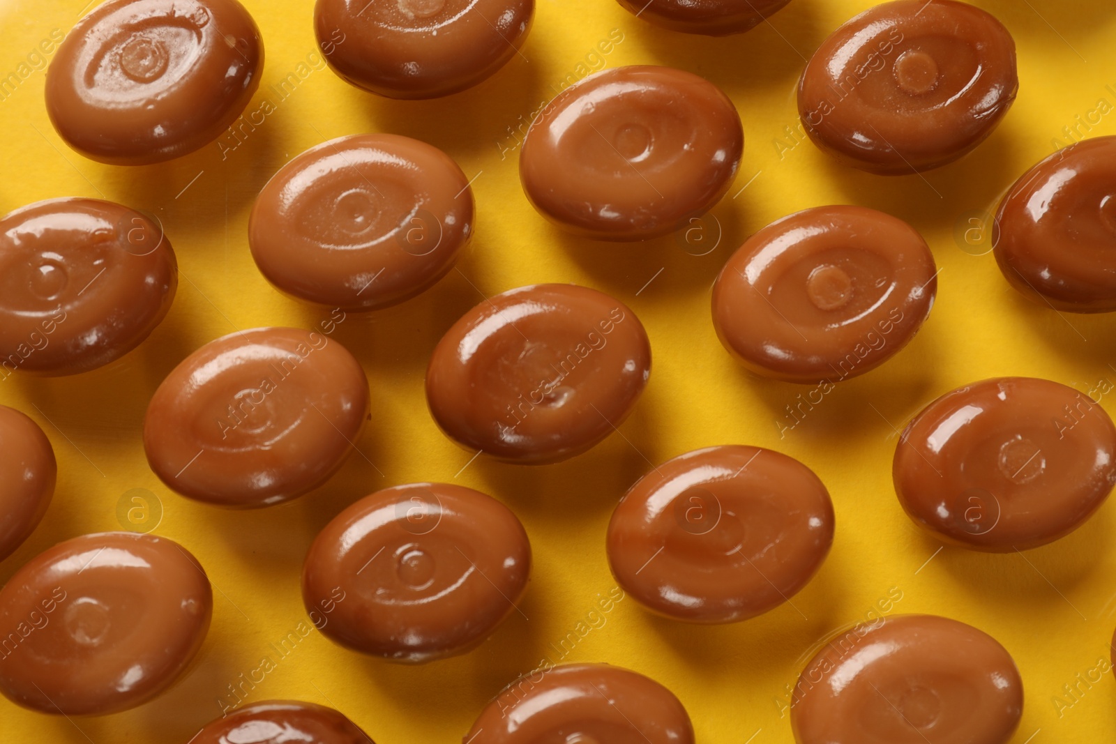 Many tasty caramel candies on yellow background, flat lay Photo of Many tasty caramel candies on yellow background, flat lay