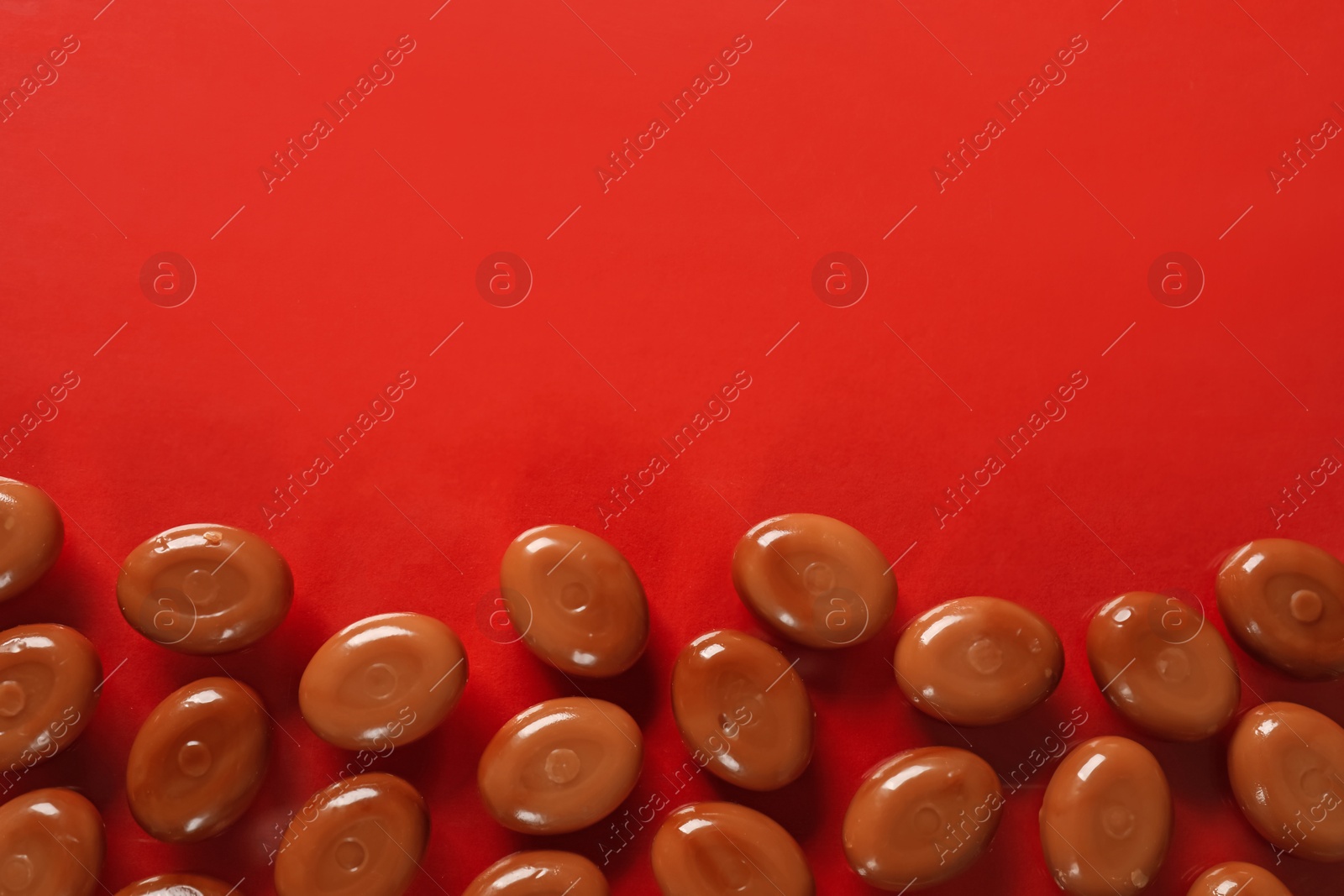 Many tasty caramel candies on red background, flat lay. Space for text Photo of Many tasty caramel candies on red background, flat lay. Space for text