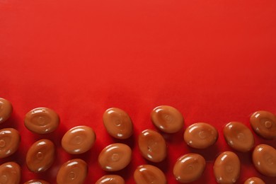 Photo of Many tasty caramel candies on red background, flat lay. Space for text