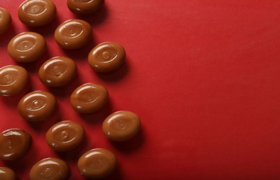 Photo of Many tasty caramel candies on red background, flat lay. Space for text