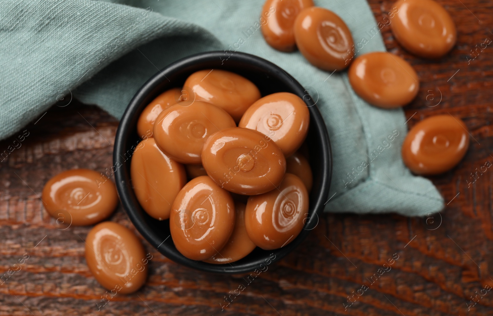 Photo of Many tasty caramel candies on wooden table, flat lay