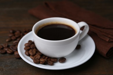 Photo of Aromatic coffee in cup, beans and saucer on wooden table, closeup