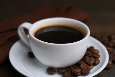 Photo of Aromatic coffee in cup, beans and saucer on wooden table, closeup