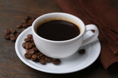 Photo of Aromatic coffee in cup, beans and saucer on wooden table, closeup