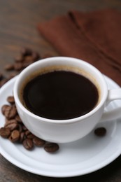Photo of Aromatic coffee in cup, beans and saucer on wooden table, closeup