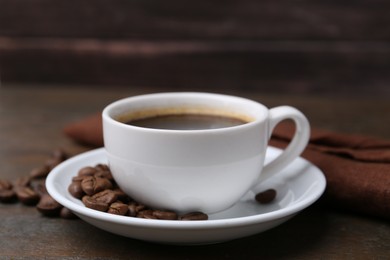 Photo of Aromatic coffee in cup, beans and saucer on wooden table, closeup