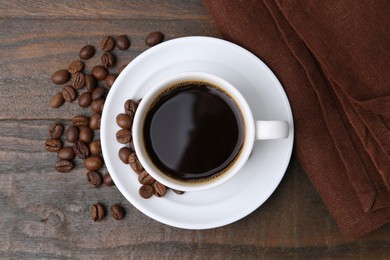 Photo of Aromatic coffee in cup, beans and saucer on wooden table, flat lay
