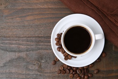 Photo of Aromatic coffee in cup, beans and saucer on wooden table, flat lay. Space for text