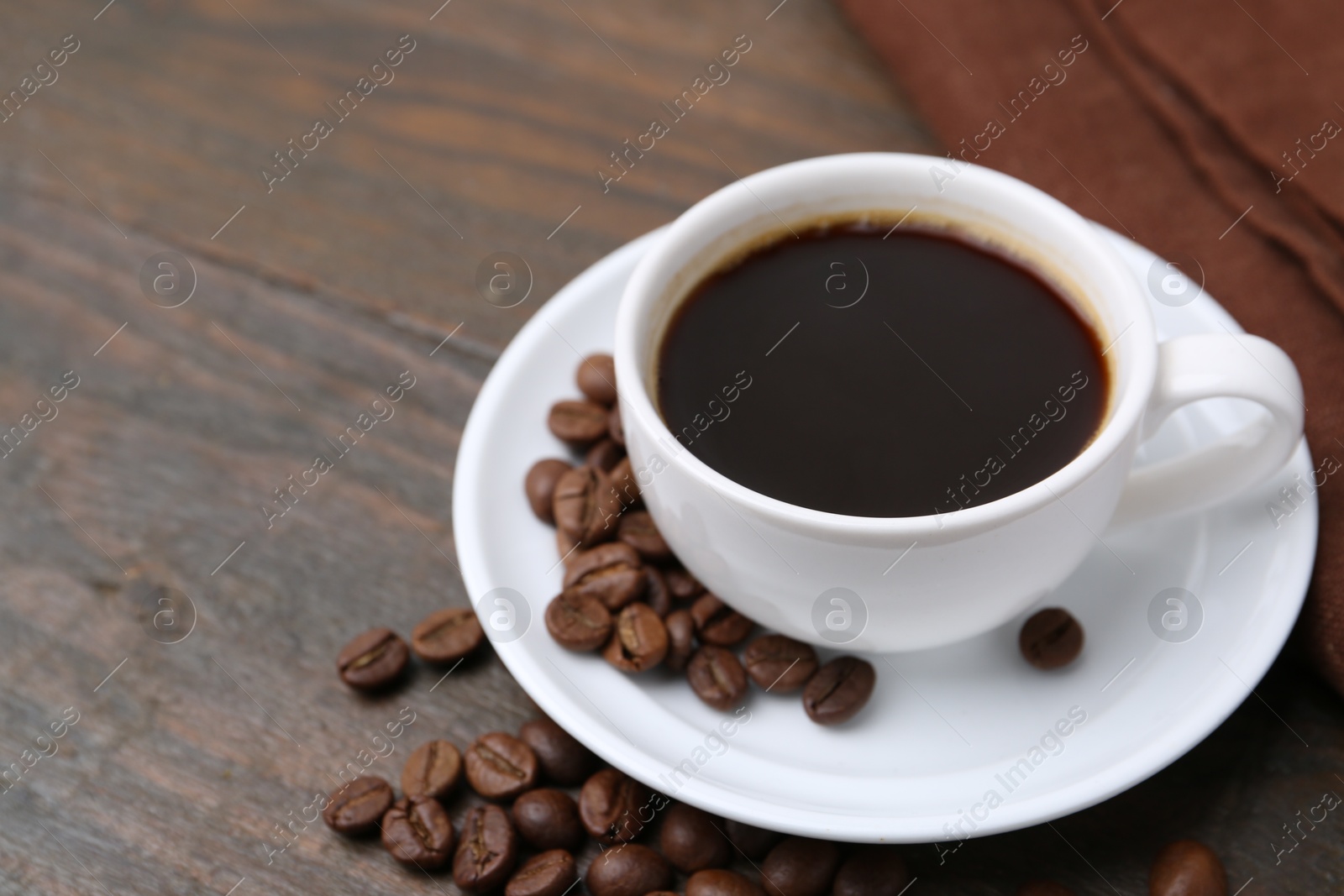 Aromatic coffee in cup, beans and saucer on wooden table, closeup. Space for text Photo of Aromatic coffee in cup, beans and saucer on wooden table, closeup. Space for text