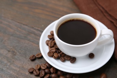 Photo of Aromatic coffee in cup, beans and saucer on wooden table, closeup. Space for text