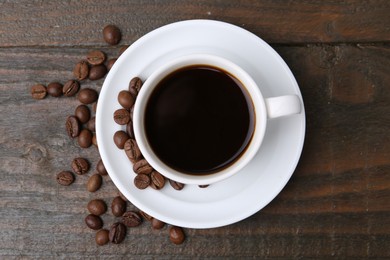Photo of Aromatic coffee in cup, beans and saucer on wooden table, flat lay