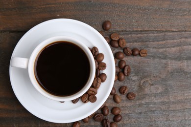 Photo of Aromatic coffee in cup, beans and saucer on wooden table, flat lay