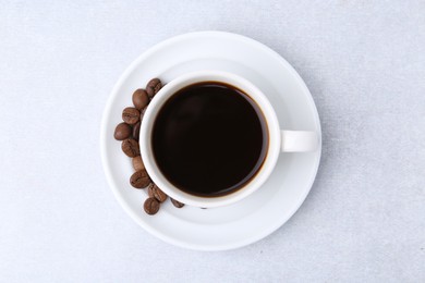 Photo of Aromatic coffee in cup, beans and saucer on light table, top view