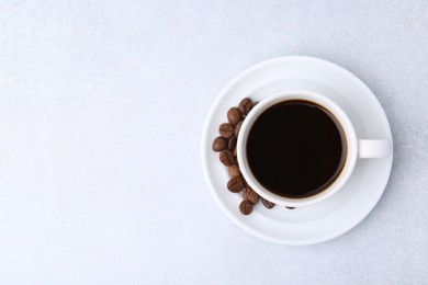 Photo of Aromatic coffee in cup, beans and saucer on light table, top view. Space for text