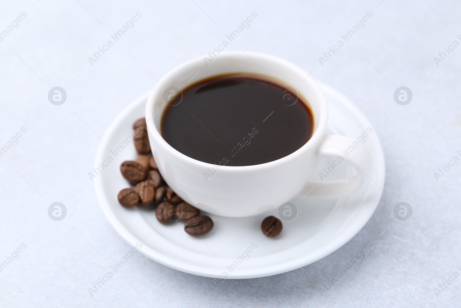Aromatic coffee in cup, beans and saucer on light table, closeup Photo of Aromatic coffee in cup, beans and saucer on light table, closeup