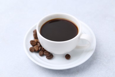 Photo of Aromatic coffee in cup, beans and saucer on light table, closeup