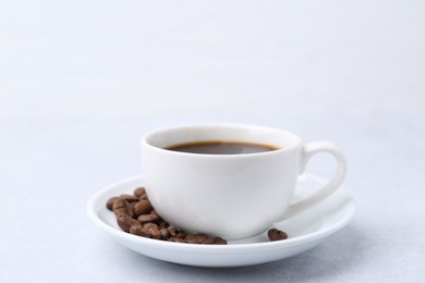 Photo of Aromatic coffee in cup, beans and saucer on light table, closeup