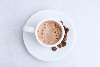 Photo of Aromatic coffee in cup, beans and saucer on light table, top view