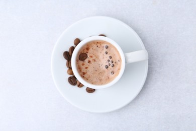 Photo of Aromatic coffee in cup, beans and saucer on light table, top view