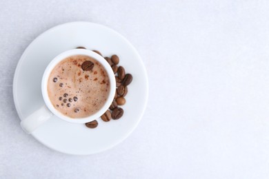 Photo of Aromatic coffee in cup, beans and saucer on light table, top view. Space for text