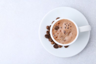 Photo of Aromatic coffee in cup, beans and saucer on light table, top view. Space for text