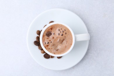 Photo of Aromatic coffee in cup, beans and saucer on light table, top view