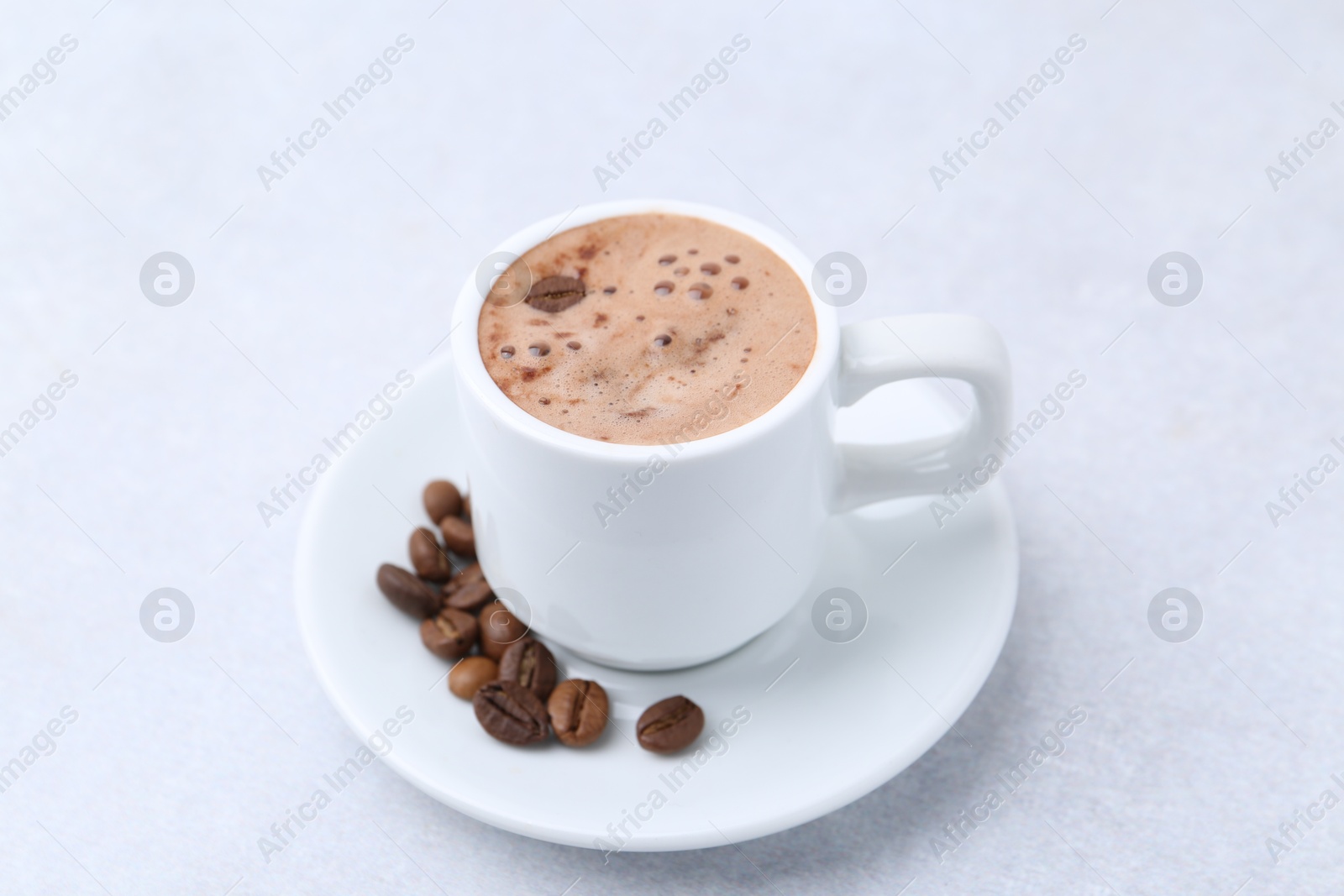 Aromatic coffee in cup, beans and saucer on light table, closeup Photo of Aromatic coffee in cup, beans and saucer on light table, closeup