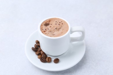 Photo of Aromatic coffee in cup, beans and saucer on light table, closeup