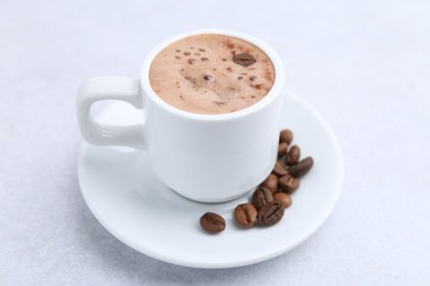 Photo of Aromatic coffee in cup, beans and saucer on light table, closeup