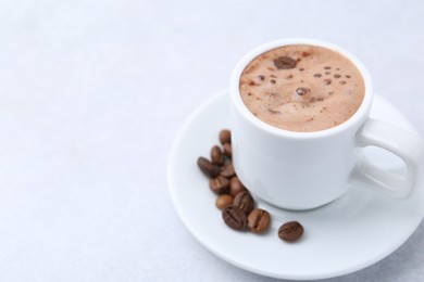 Photo of Aromatic coffee in cup, beans and saucer on light table, closeup. Space for text