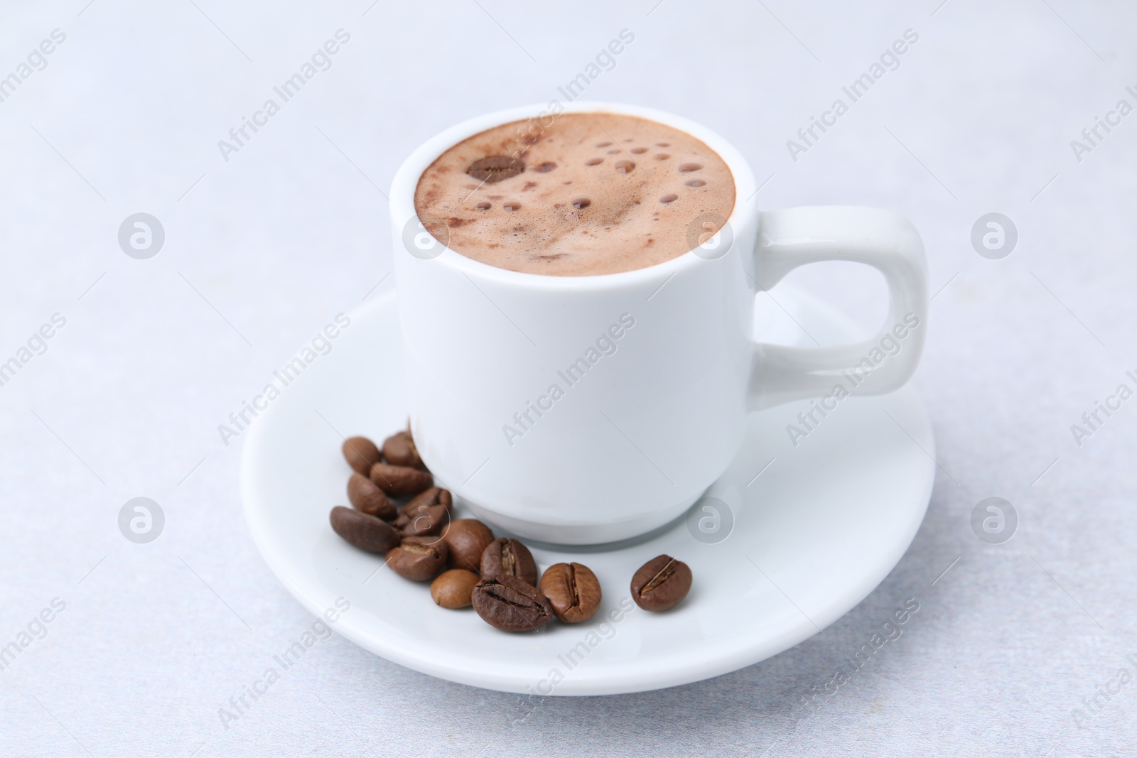 Aromatic coffee in cup, beans and saucer on light table, closeup Photo of Aromatic coffee in cup, beans and saucer on light table, closeup