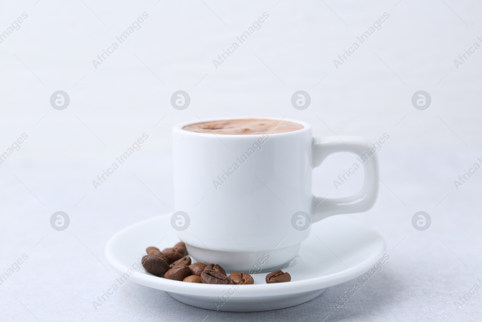 Aromatic coffee in cup, beans and saucer on light table, closeup Photo of Aromatic coffee in cup, beans and saucer on light table, closeup