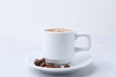 Photo of Aromatic coffee in cup, beans and saucer on light table, closeup