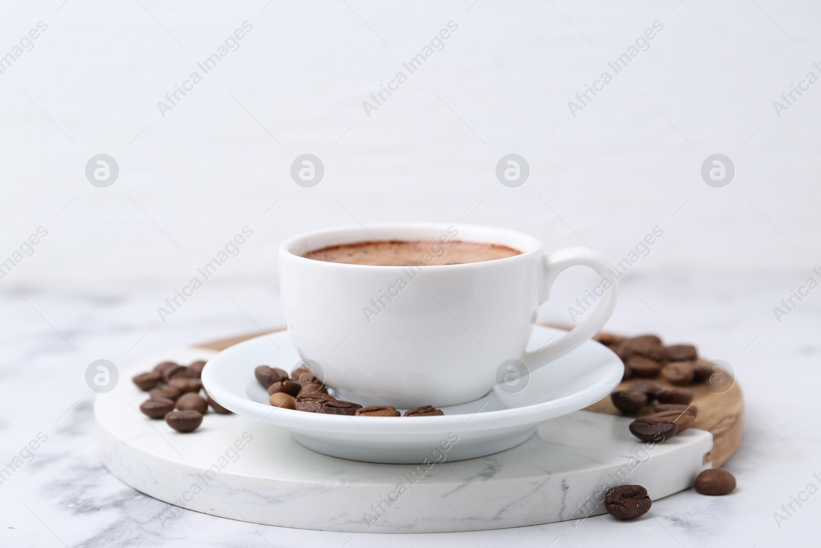 Aromatic coffee in cup, beans and saucer on white marble table, closeup Photo of Aromatic coffee in cup, beans and saucer on white marble table, closeup