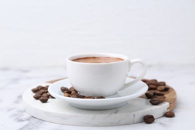 Photo of Aromatic coffee in cup, beans and saucer on white marble table, closeup