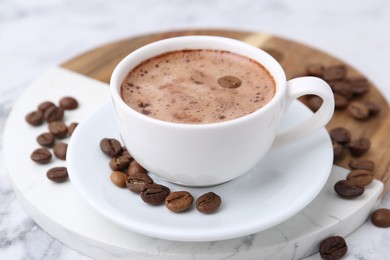 Photo of Aromatic coffee in cup, beans and saucer on white marble table, closeup