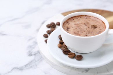Photo of Aromatic coffee in cup, beans and saucer on white marble table, closeup. Space for text