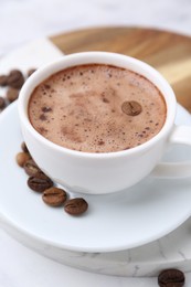 Photo of Aromatic coffee in cup, beans and saucer on white table, closeup