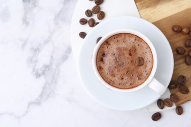 Photo of Aromatic coffee in cup, beans and saucer on white marble table, top view. Space for text