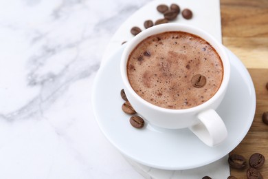 Photo of Aromatic coffee in cup, beans and saucer on white marble table, closeup. Space for text