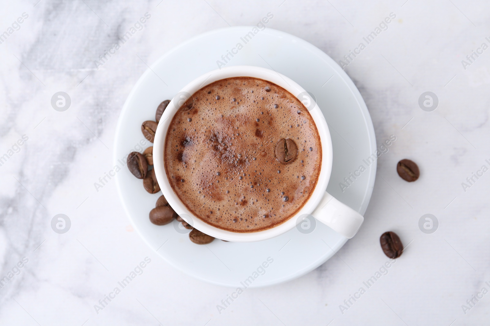 Aromatic coffee in cup, beans and saucer on white marble table, top view Photo of Aromatic coffee in cup, beans and saucer on white marble table, top view