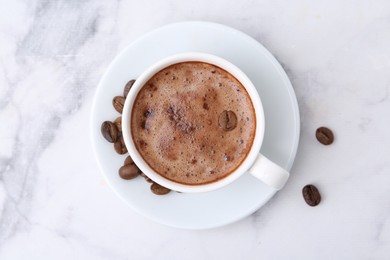 Photo of Aromatic coffee in cup, beans and saucer on white marble table, top view