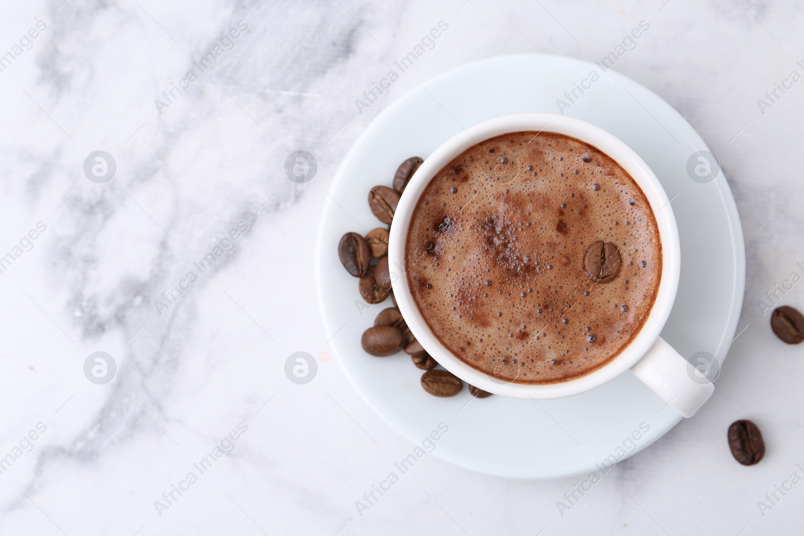 Aromatic coffee in cup, beans and saucer on white marble table, top view. Space for text Photo of Aromatic coffee in cup, beans and saucer on white marble table, top view. Space for text