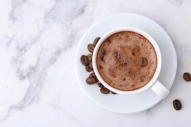 Photo of Aromatic coffee in cup, beans and saucer on white marble table, top view. Space for text